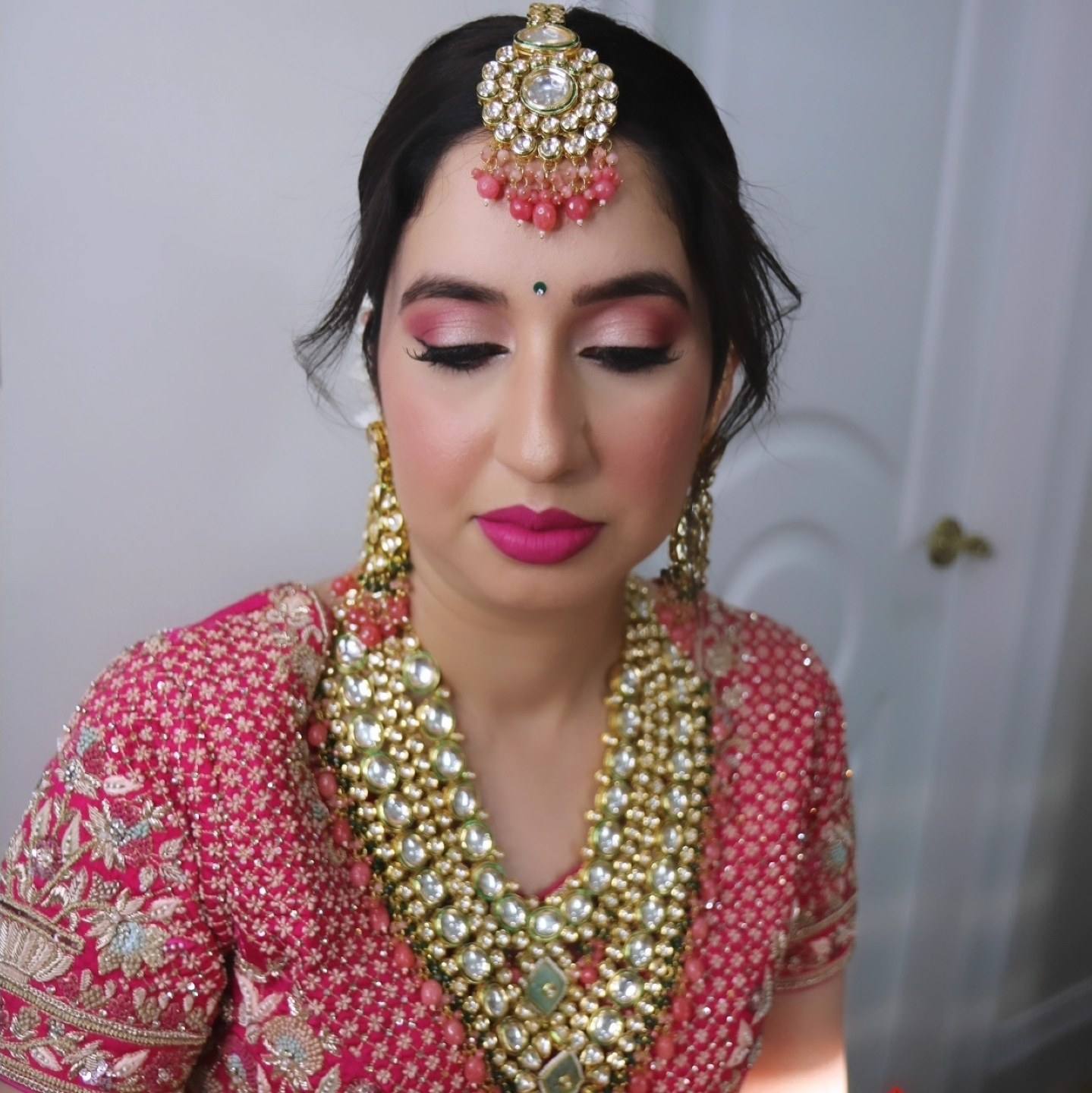 Bride in a pink lehenga with gold kundan jewellery, maang tikka and soft glam makeup