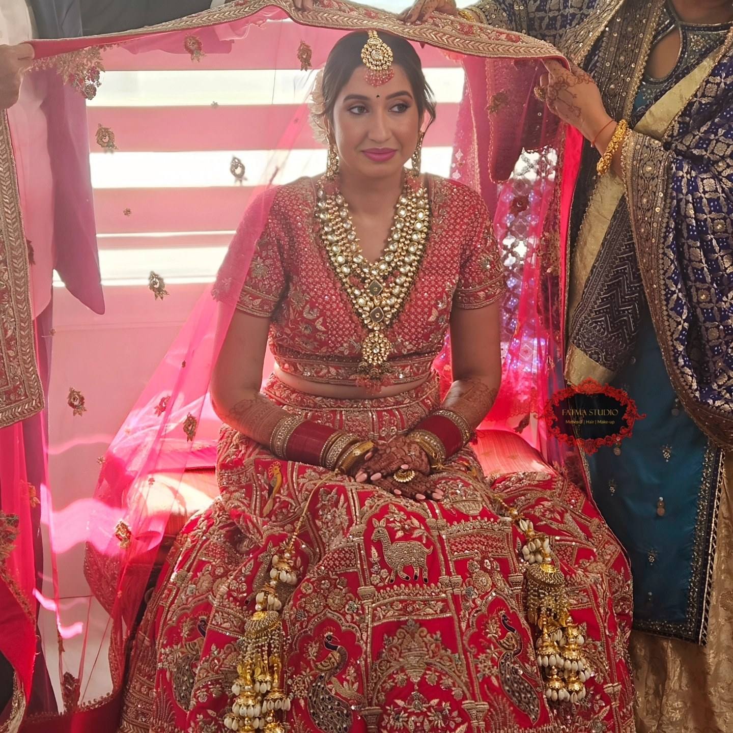 Seated bride in a red and gold lehenga with full bridal makeup, jewellery and henna
