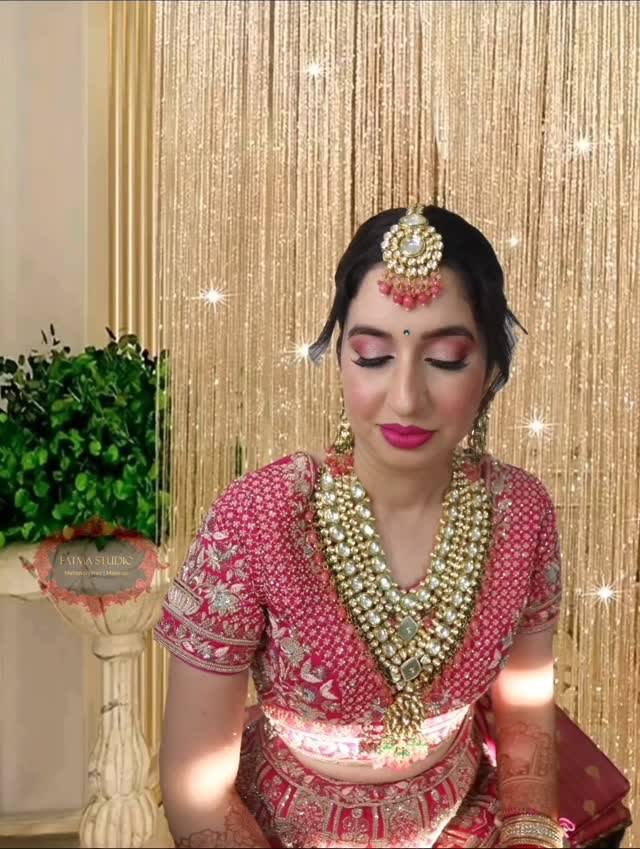Bride in a pink lehenga seated in front of a bead curtain, full bridal look