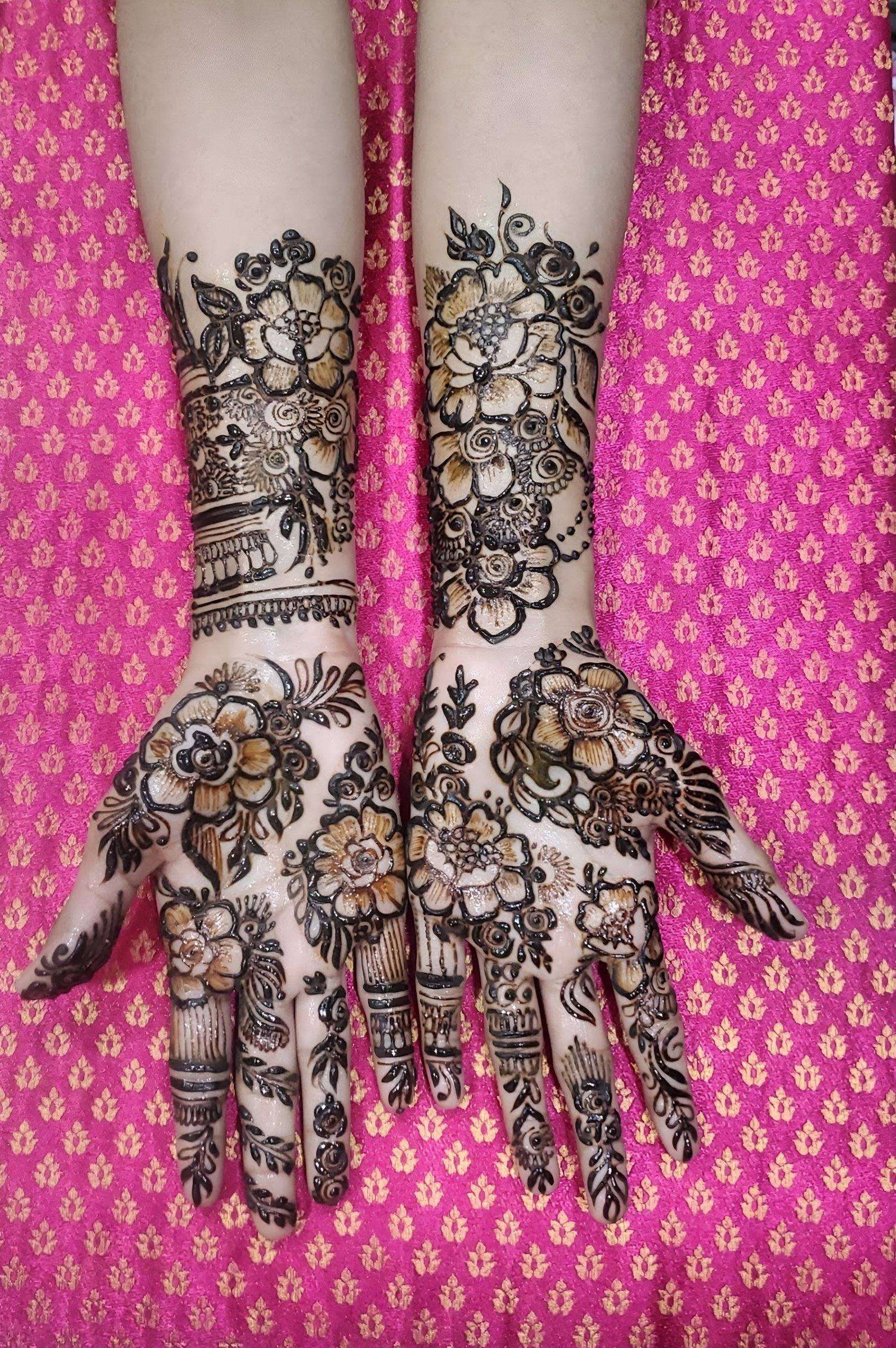 Floral shaded henna on hands and wrists over pink patterned fabric