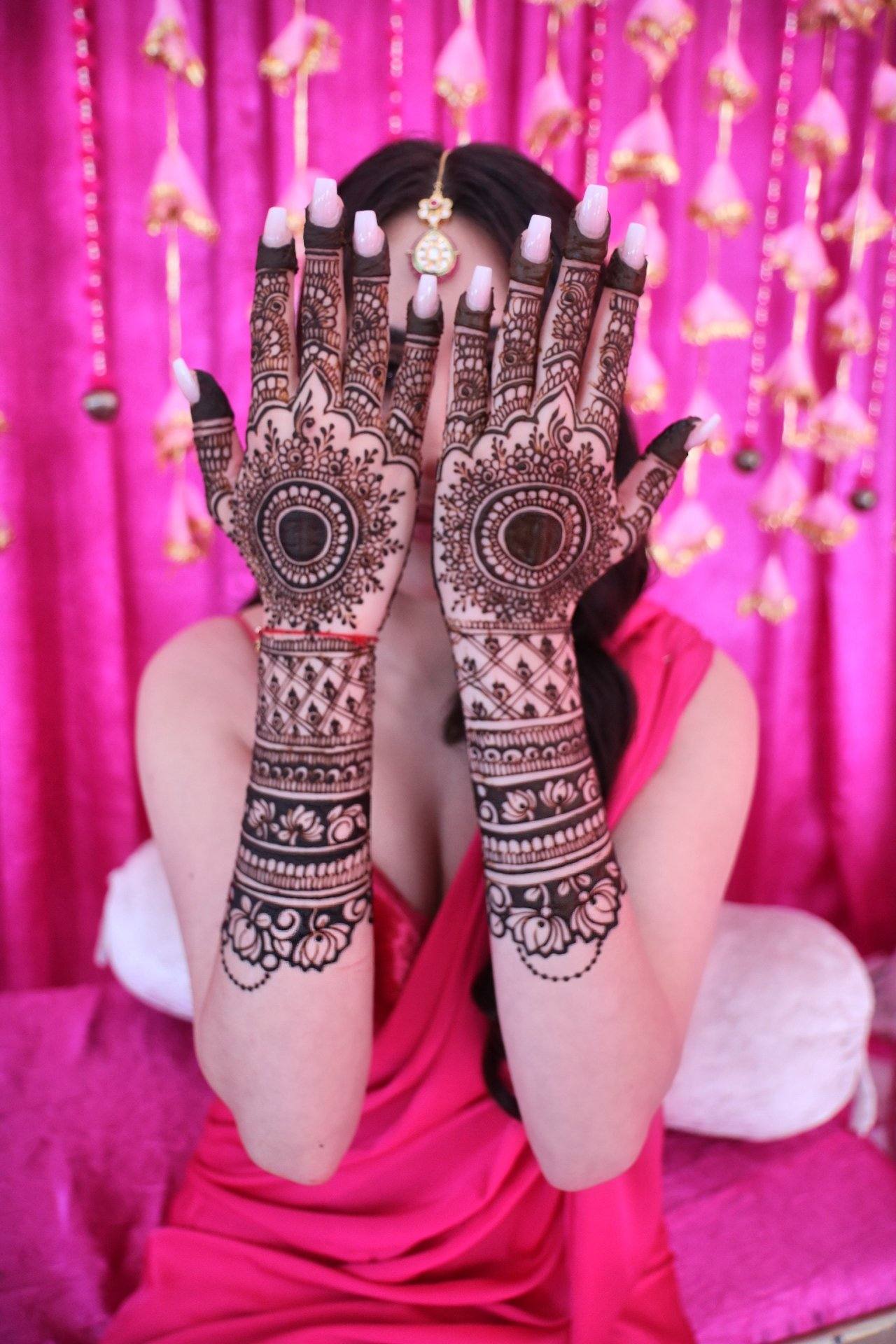 Bride in pink hiding her face behind henna-covered hands in front of floral decor