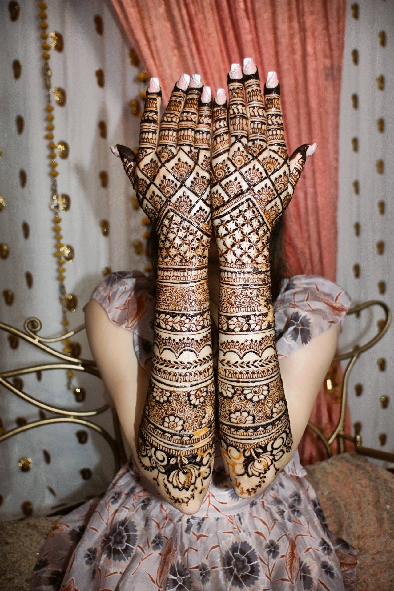 Bride raising henna-covered arms in front of her face against a gold-dotted backdrop