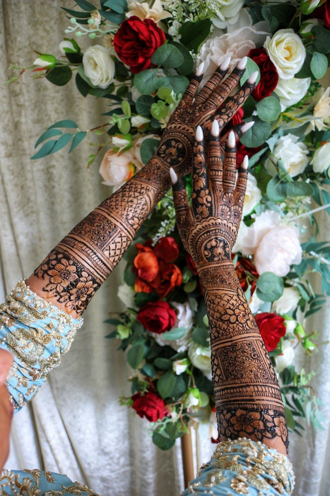 Bridal henna arms posed against a wall of red and white roses