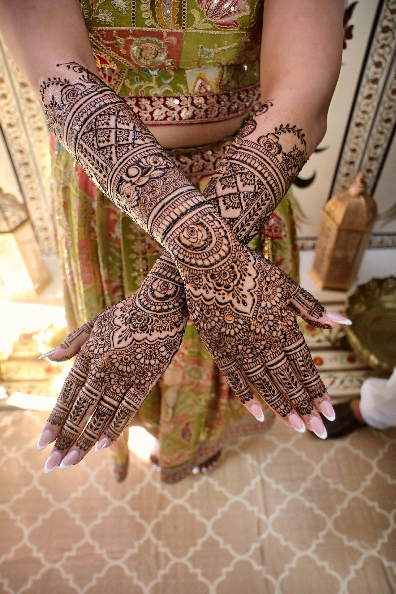 Bride with crossed arms showing full henna over a green outfit