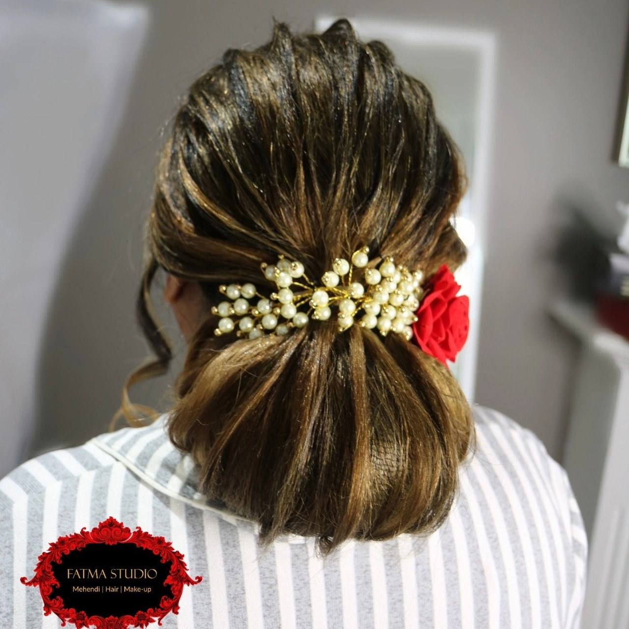 Low bun finished with pearl hairpins and a red flower
