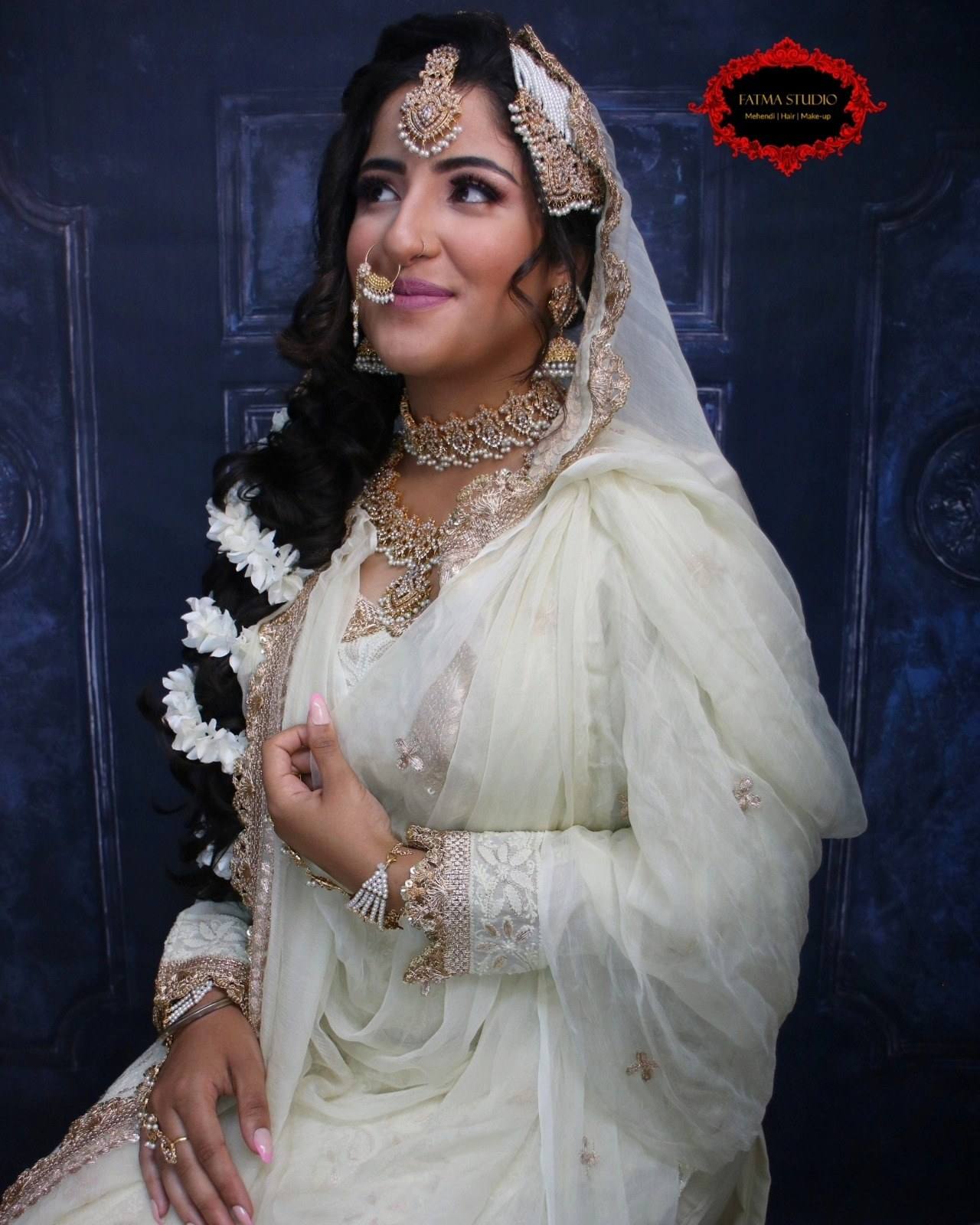 Bride in an ivory outfit with a nose ring, bold eye makeup and jasmine-wrapped curled hair